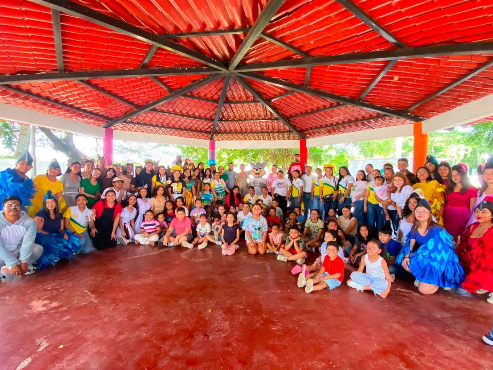 Grupo de estudiantes, docentes, niñas y niños posa bajo una palapa después de una actividad de Cuenta Cuentos.